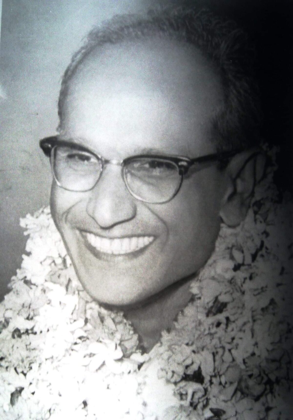 Close portrait of a smiling Batukeshwar Dutt in later life, wearing spectacles and a thick flower garland.